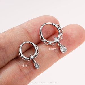 May include: Two silver hoop earrings with a teardrop-shaped crystal dangle. The smaller hoop is 8mm in diameter and the larger hoop is 10mm in diameter.