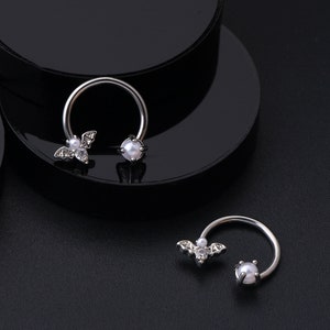 May include: Two silver horseshoe shaped rings with a pearl and a bat charm. The bat charm has a small pearl in the center.