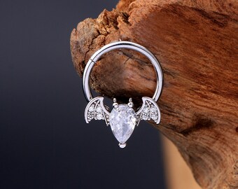 Puede incluir: Anillo de septum de plata con un dije de murciélago de cristal transparente. El murciélago tiene alas con pequeños cristales transparentes.