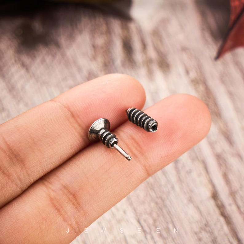 May include: Two silver-colored screw-shaped earrings. One earring has a post and a decorative head, while the other is a cylindrical screw. The earrings are designed to look like miniature screws.