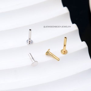 Op de afbeelding: Drie 14 karaats gouden en roestvrijstalen neusstuds. De studs zijn in verschillende kleuren, een is goud, een is zilver en een is een combinatie van goud en zilver. De studs zijn allemaal even groot en hebben dezelfde vorm, met een platte bovenkant en een lange, dunne schacht.