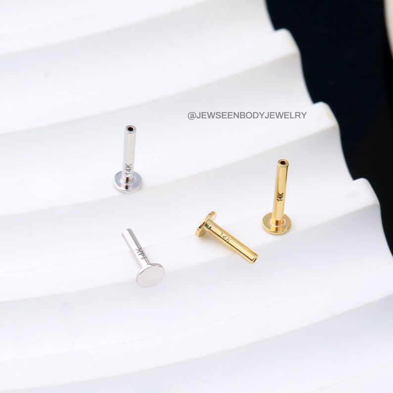 Op de afbeelding: Drie 14 karaats gouden en roestvrijstalen neusstuds. De studs zijn in verschillende kleuren, een is goud, een is zilver en een is een combinatie van goud en zilver. De studs zijn allemaal even groot en hebben dezelfde vorm, met een platte bovenkant en een lange, dunne schacht.