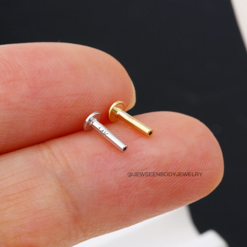 Op de afbeelding: Twee gouden lichaamsieraden, een is goud en de andere is zilver. Beide zijn gemarkeerd met "14K".