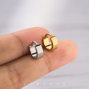 Puede incluir: Se muestran dos pequeños pendientes de aro, uno plateado y otro dorado. Los pendientes tienen un diseño sencillo y moderno con una parte delantera rectangular. La palabra "JEWSEEN" es visible en la parte inferior de la imagen.