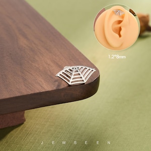 Op de afbeelding: Een zilveren oorbel in de vorm van een waaier, afgebeeld op een houten oppervlak. De oorbel is 1,2 mm bij 8 mm. Het woord "JEWSEEN" staat onderaan de afbeelding.