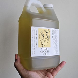 Könnte beinhalten: Ein durchsichtiger Plastikkanister gefüllt mit gelber Flüssigkeit, beschriftet mit "Hair Growth Oil". Das Etikett enthält auch Gebrauchsanweisungen und eine Zutatenliste.