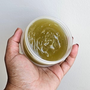 May include: A clear plastic container with a green, gel-like substance inside. The container is being held in a person's hand.