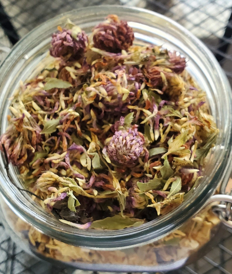 Puede incluir: Un tarro de vidrio lleno de flores de tr&eacute;bol p&uacute;rpura secas y hojas verdes. El tarro est&aacute; lleno hasta el borde con las flores y hojas secas.
