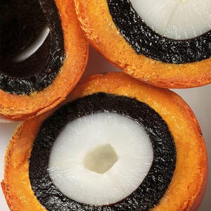 Pode incluir: Close-up de tr&ecirc;s peda&ccedil;os de fruta, cada um cortado para revelar uma se&ccedil;&atilde;o transversal. A fruta tem um centro branco, um anel preto e uma camada externa laranja. As pe&ccedil;as s&atilde;o dispostas sobre um fundo branco.