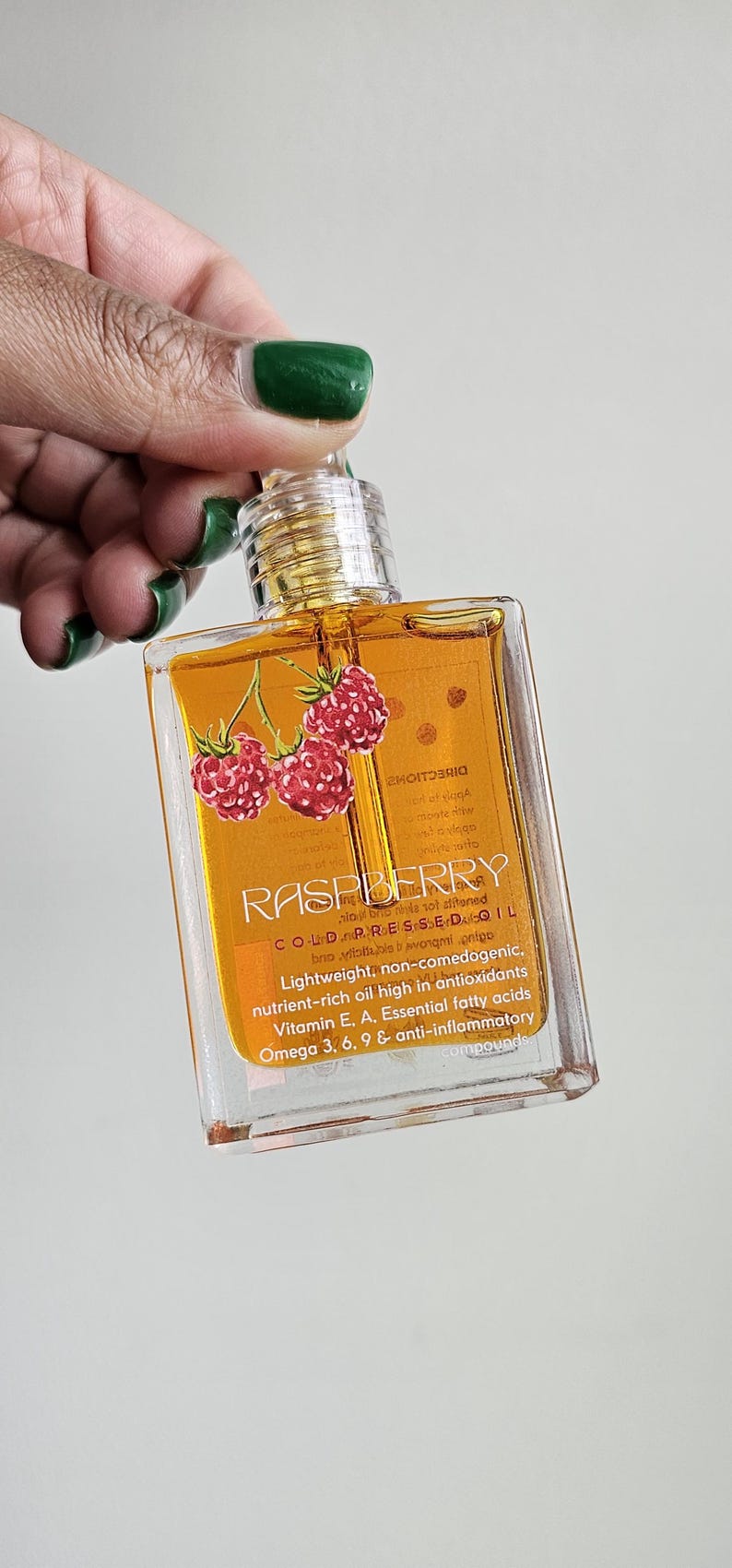 Puede incluir: Una botella cuadrada transparente de aceite de frambuesa con tapa dorada. La etiqueta presenta la palabra "RASPBERRY" y un gr&aacute;fico de tres frambuesas rojas. La botella contiene un l&iacute;quido dorado.