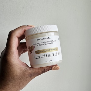 May include: A jar of Monoi De Tahiti oil by The Batana Co. is held in a hand. The label reads "Raw & Cold Pressed" and lists ingredients. The jar is white with a white lid and contains 8 fl oz / 236 mL of product.