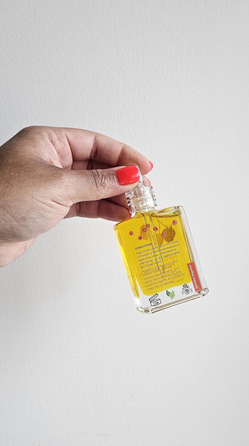 Puede incluir: Una botella rectangular transparente llena de l&iacute;quido amarillo, sostenida por una mano con esmalte de u&ntilde;as rojo. La botella tiene una tapa transparente y una etiqueta con texto e ilustraciones de bayas. La etiqueta dice "Kentry Organics".