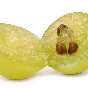 May include: A close-up of a halved green grape, revealing the juicy interior and two brown seeds. The translucent flesh of the grape is a pale green color, with a glistening texture. The background is white.
