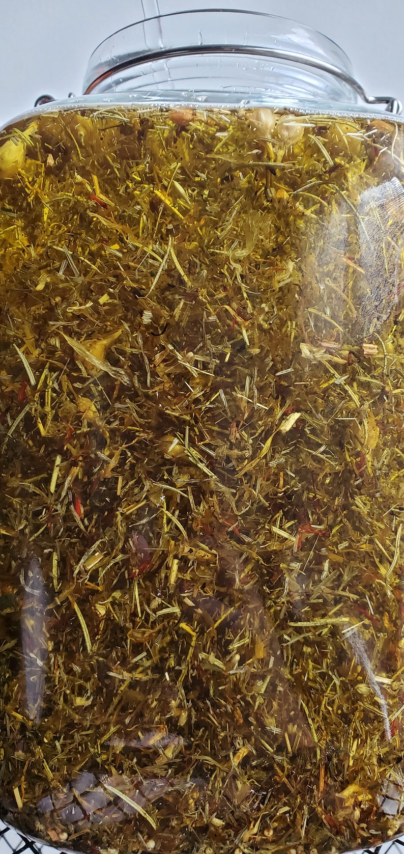 Puede incluir: Un frasco de vidrio lleno de hierbas y flores secas, sumergidas en un l&iacute;quido transparente. Las hierbas y las flores son una mezcla de verde, amarillo y rojo.