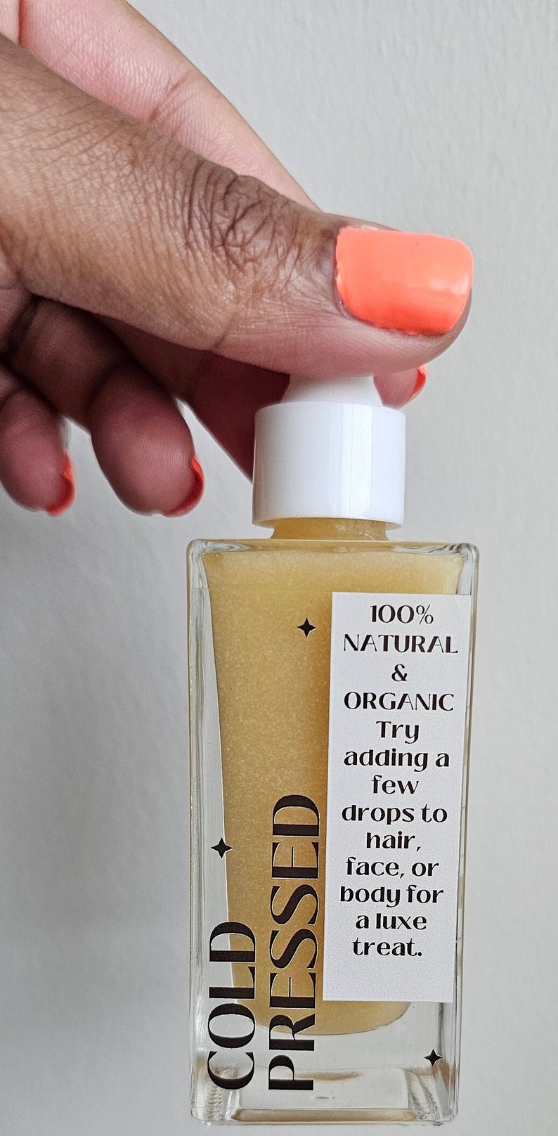 May include: A clear glass bottle with a white dropper top filled with a golden liquid. The label reads "COLD PRESSED" and "100% NATURAL & ORGANIC. Try adding a few drops to hair, face, or body for a luxe treat."