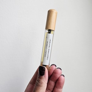 Może przedstawiać: Przezroczysta butelka ze szklanym korkiem z drewna, zawierająca odżywkę do rzęs i brwi. Butelka jest oznaczona etykietą "Eyelash + Eyebrow Conditioning Treatment".