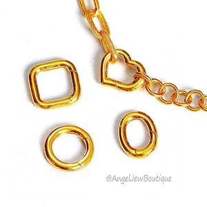 Könnte beinhalten: Goldfarbene Schmuckkette mit einem herzförmigen Anhänger und drei Sprungringen. Die Sprungringe haben verschiedene Formen, darunter ein Quadrat und zwei Kreise.