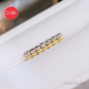 May include: A gold and silver-toned jewellery piece with a repeating bead design. The piece is set against a white background. A red circle with the text "G18K" is in the upper left corner.
