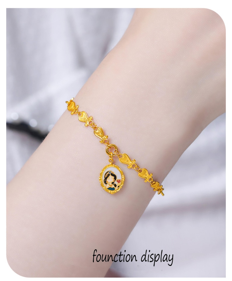 May include: A gold-toned chain bracelet featuring a series of small, repeating decorative links and a single oval pendant. The pendant displays a colorful enamel illustration of a character with dark hair and a blue outfit set within a gold frame.