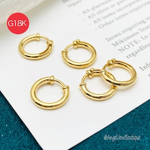 Puede incluir: Cuatro pendientes de aro dorados con acabado pulido. Los pendientes son circulares y cuentan con un mecanismo de cierre de bisagra. Un gráfico circular rojo en la esquina superior izquierda contiene el texto blanco G18K. Joyas sobre papel blanco.