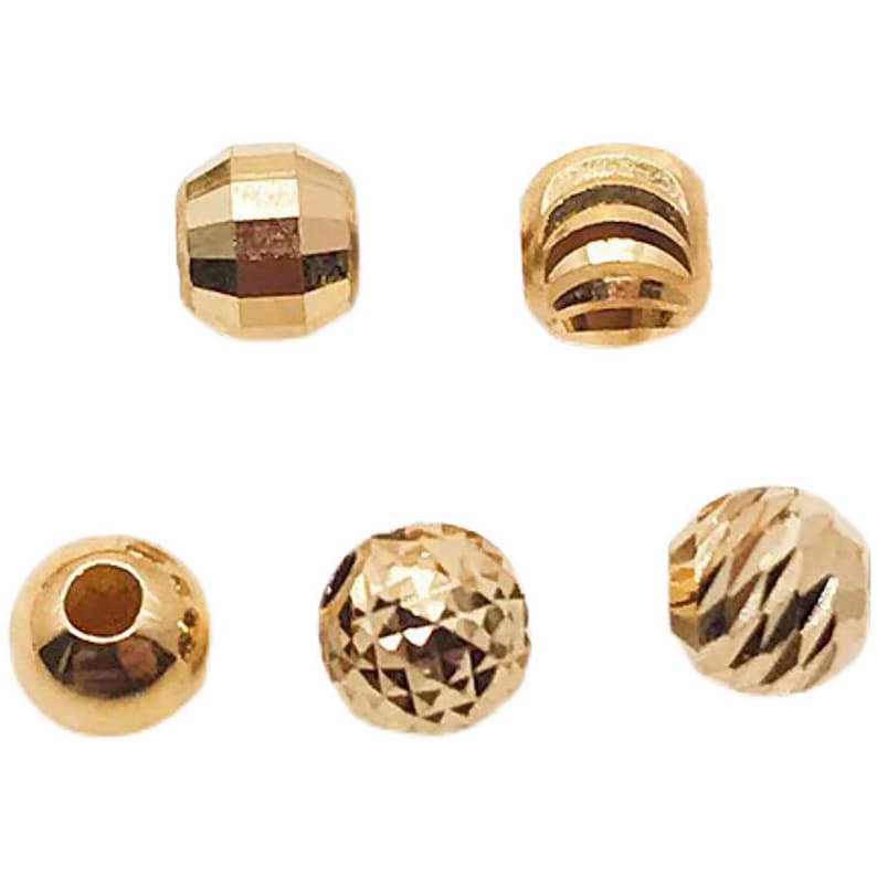Peut inclure: Cinq perles dor&eacute;es de diff&eacute;rentes formes. Les perles comprennent des motifs &agrave; facettes, &agrave; ar&ecirc;tes et sph&eacute;riques. Les perles sont probablement destin&eacute;es &agrave; la fabrication de bijoux ou &agrave; l'artisanat. Les perles sont pr&eacute;sent&eacute;es sur fond blanc.