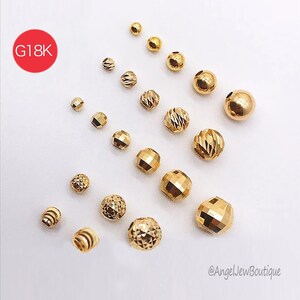 Peut inclure: Diverses perles dor&eacute;es de diff&eacute;rentes tailles et formes facett&eacute;es, dispos&eacute;es sur une surface blanche. Un cercle rouge avec "G18K" est en haut &agrave; gauche. L'image met en valeur l'&eacute;clat des perles. Les perles sont mesur&eacute;es en millim&egrave;tres.