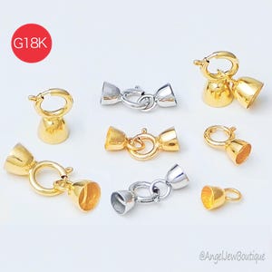 May include: An assortment of gold and silver-toned jewelry clasps. The clasps feature a bell-shaped design with a ring and clasp closure. The image includes a red circle with the text "G18K". The clasps are displayed on a white background.