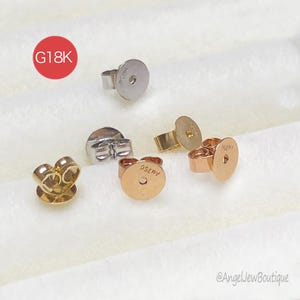 Puede incluir: Una variedad de cierres de pendientes en tonos oro, oro rosa y plata. La imagen incluye varios estilos, como mariposas y discos. El texto "G18K" es visible en un círculo rojo. El texto "AU750" está estampado en algunos cierres.