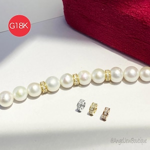Op de afbeelding: Een parelketting met gouden en diamanten details. De ketting heeft grote, ronde, witte parels gescheiden door gouden banden bezet met kleine diamanten. Drie extra gouden en zilveren diamanten ringen worden eronder weergegeven.