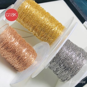 May include: Three spools of chain in gold, rose gold, and silver tones. The gold chain is labeled "G18K" in a red circle. The chains are displayed on white plastic holders, with the @AngelJewBoutique watermark in the bottom right corner.