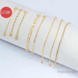 May include: A collection of gold-colored chain extenders in various designs, including beaded, oval link, and curb chain styles. Each extender features a clasp at both ends for easy attachment. The image includes a red circle with the text "G18K".