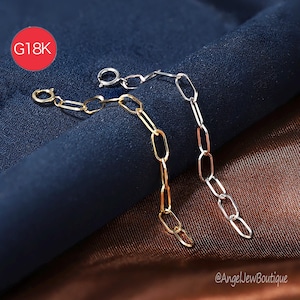 May include: Two delicate chain extenders, one gold and one silver, with elongated oval links. The chains are displayed against a dark blue and brown textured background. A red circle with "G18K" is in the upper left corner.