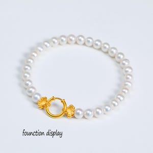 May include: A white pearl bracelet featuring a circular gold-toned clasp mechanism with two small cloud-shaped gold-toned accents on either side. The text founction display is printed in black in the lower left corner of the image.
