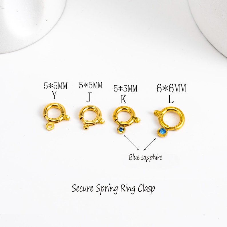 May include: Four gold-colored spring ring clasps, with sizes and letters labeled. One clasp has a blue sapphire. The text "Secure Spring Ring Clasp" is below the clasps.