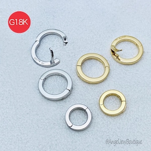 May include: A selection of gold and silver hoop earrings. The earrings are circular, featuring a hinged clasp design. One earring is open, revealing the clasp mechanism. The image includes a red circle with the text "G18K".