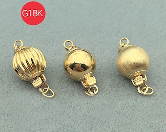 May include: Three gold-colored jewelry clasps. The clasps have a round shape with different surface textures: ribbed, smooth, and matte. Each clasp has a small loop at the top and a hinged closure at the bottom. The clasps are displayed on a gray surface.