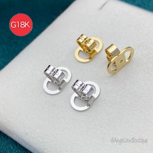 Op de afbeelding: Close-up van vier oorbelruggen in goud- en zilverkleuren. Twee zijn goudkleurig en twee zijn zilverkleurig. De oorbelruggen hebben een pin en een vlindersluiting. De afbeelding bevat een rode cirkel met de tekst "G18K".