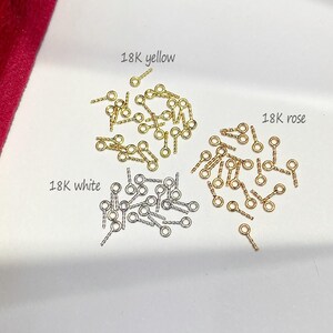 May include: Close-up of three piles of small jewelry findings. The findings are in 18K yellow, white, and rose gold. Each finding has a small loop and a textured stem. The text "18K yellow", "18K white", and "18K rose" are above each pile.