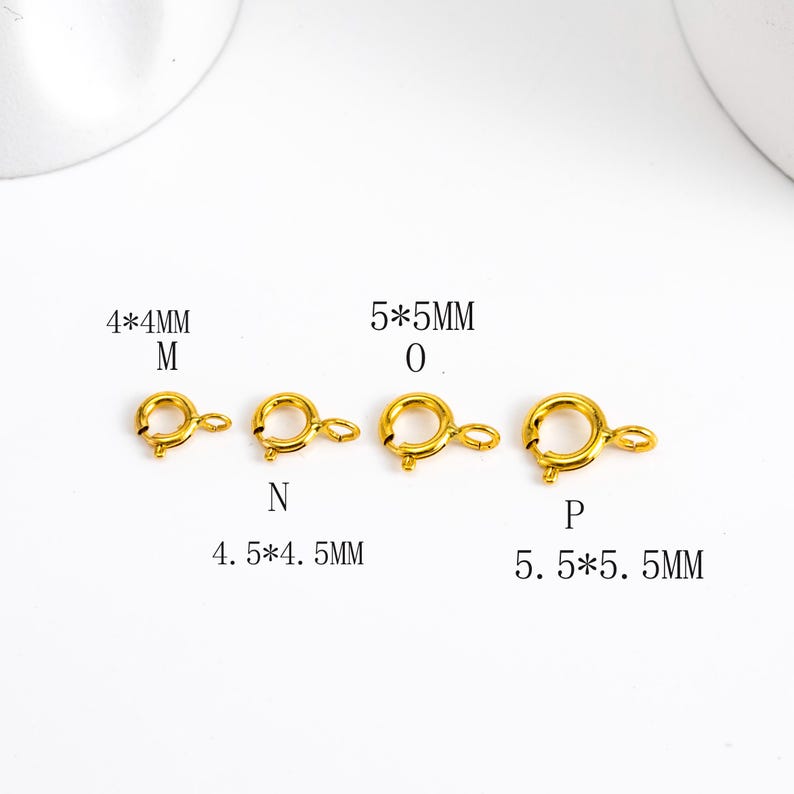 May include: Four gold-colored spring clasp jewelry findings in varying sizes. The smallest is 4x4mm, and the largest is 5.5x5.5mm. Each clasp has a circular ring and a lever for secure closure. Text indicates sizes.