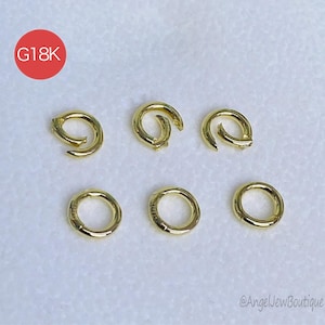 Può includere: Sei chiusure per gioielli color oro di varie forme. Tre sono circolari e tre sono curve. Un cerchio rosso con la scritta "G18K" si trova nell'angolo in alto a sinistra. Le chiusure sono su uno sfondo chiaro.