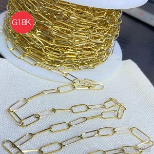 May include: A spool of gold-colored chain with a paperclip link design. The chain is displayed on a white spool and a white cloth. A red circle with the text "G18K" is visible.
