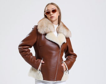 May include: A brown leather jacket with a white fur collar and a zipper closure. The jacket has two pockets on the front and a white fur lining. The model is wearing white pants and brown boots.