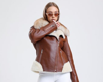 May include: A brown leather jacket with a white fur collar and a zipper closure. The jacket is worn by a person with white pants and brown boots.
