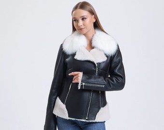May include: A black leather jacket with a white fur collar and trim. The jacket has a zipper closure and a  zippered pocket on the left sleeve. The model is wearing blue jeans and white sneakers.