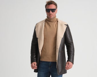May include: A man wearing a brown leather jacket with a shearling collar, blue jeans, and white sneakers. He is wearing black sunglasses and a brown turtleneck sweater.