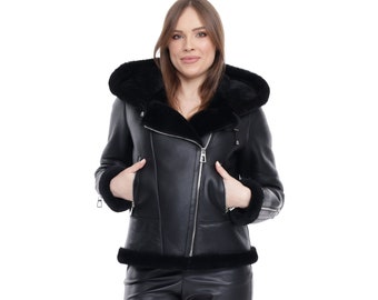 May include: A black leather jacket with a fur-lined hood. The jacket has a zipper closure and two pockets. The model is wearing black leather shorts and black ankle boots.