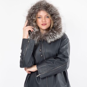 May include: A dark blue leather jacket with a fur-lined hood. The jacket has a zipper closure, zippered sleeves, and a dark blue suede trim at the bottom. The hood features a mix of brown and silver fur.