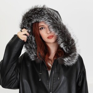 May include: A black leather jacket with a fur-lined hood. The hood is pulled up over the head of the person wearing the jacket. The fur is a light gray color.