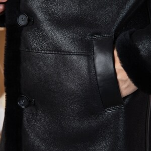 Puede incluir: Una chaqueta de cuero negra con forro de piel de oveja. La chaqueta tiene un bolsillo de solapa en el lado izquierdo y un cierre de bot&oacute;n.