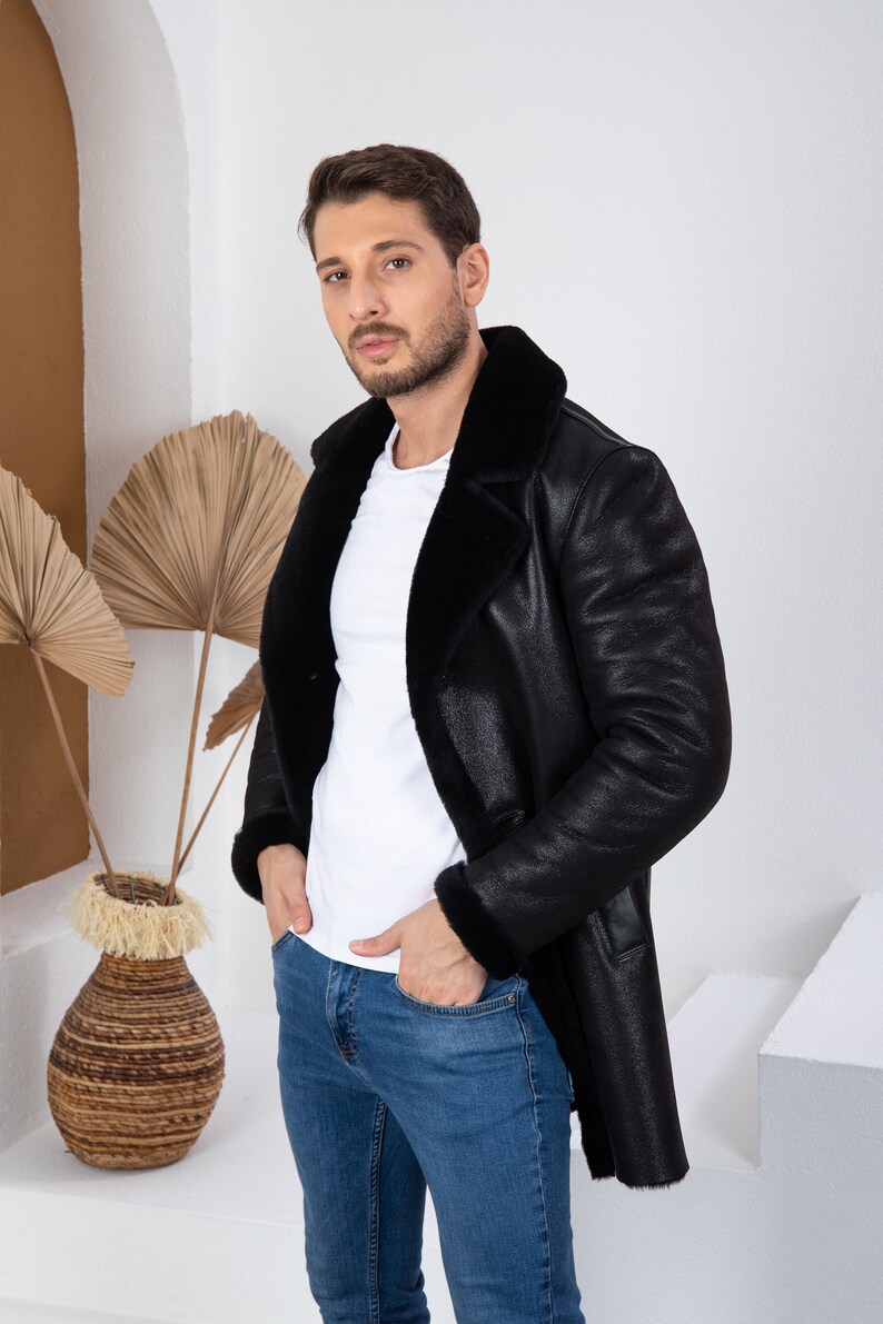 Puede incluir: Un hombre con una chaqueta de cuero negra con cuello de piel y pantalones vaqueros azules. La chaqueta tiene una cremallera y dos bolsillos.